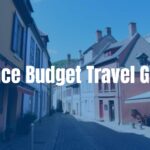 A charming French village street with colorful old houses, cobblestone path, sunny day, rustic cafe with outdoor seating, distant view of a castle on a hill, budget travel vibe.